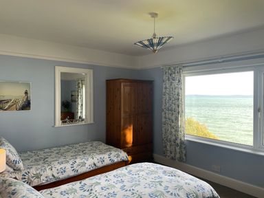 A bedroom with two single beds a wooden wardrobe a window with floral curtains and a sea view at Rocklea Seaside Cottage in Newcastle County Down