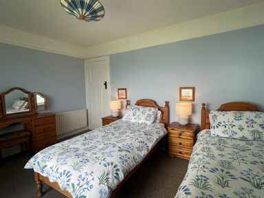 A bedroom with two single beds floral bedding lamps on wooden bedside tables and a wooden dressing table with mirror at Rocklea Seaside Cottage in Newcastle County Down
