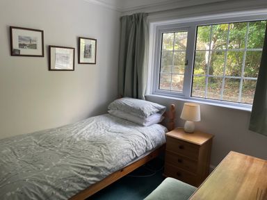 A small bedroom with a single bed a wooden nightstand with a lamp three pictures on the wall and a window with green curtains at Rocklea Seaside Cottage in Newcastle County Down