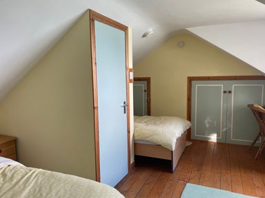 A bedroom with two beds a blue door built in cupboards and wooden floor at Rocklea Seaside Cottage in Newcastle County Down