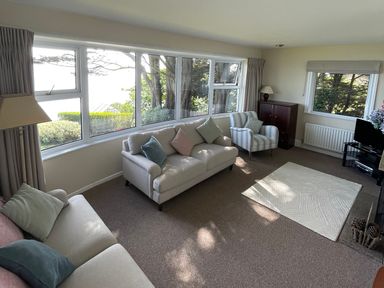 A living room with sofas pillows a lamp a chair a cabinet a TV and large windows at Rocklea Seaside Cottage in Newcastle County Down