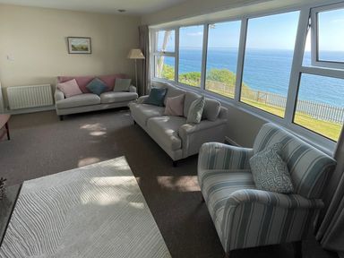 A living room with sofas and armchair facing large windows with a sea view at Rocklea Seaside Cottage in Newcastle County Down