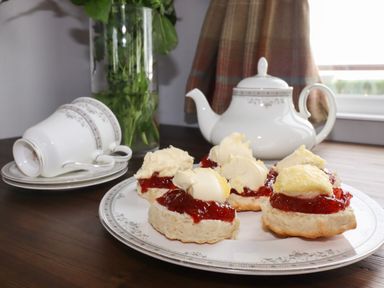 A plate with scones topped with cream and jam a teapot teacups and saucers on a wooden table at Sycamore Lodge in Porkellis near Helston
