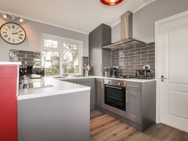 A kitchen with grey cabinets a stove oven toaster and window at Sycamore Lodge in Porkellis near Helston
