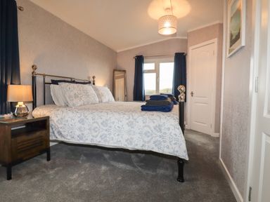 A bedroom with a bed a bedside table with lamp curtains and a window at Sycamore Lodge Porkellis near Helston