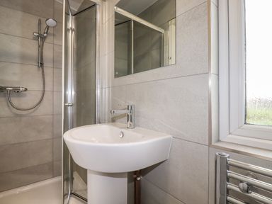 A bathroom with a shower enclosure a white sink and a window at Sycamore Lodge in Porkellis near Helston