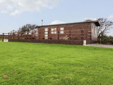 A wooden cabin with a raised deck and railing on a grassy field at Sycamore Lodge in Porkellis near Helston