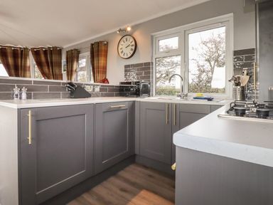 A kitchen with gray cabinets a stove a sink a microwave and plaid curtains at Sycamore Lodge Porkellis near Helston