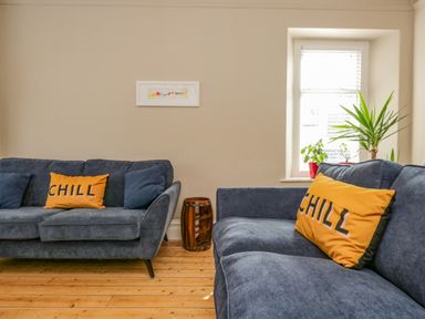 A living room with two blue sofas and yellow pillows with chill text with plants near a window at Hollywood in Windermere