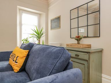 A blue sofa with a yellow pillow and green plants near a window next to a green cabinet with a mirror above it at Hollywood in Windermere