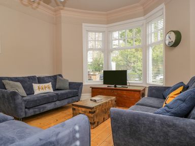 A living room with blue sofas a wooden coffee table a wooden TV stand and a wall clock at Hollywood in Windermere