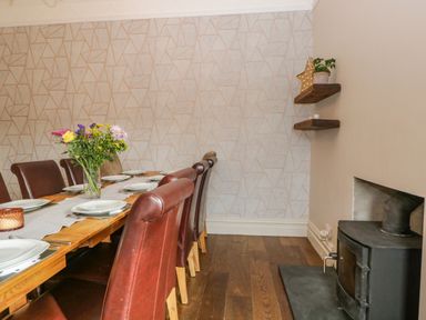 A dining room with a wooden table set with plates and a vase of flowers brown leather chairs two wooden shelves and a black wood stove at Hollywood Windermere