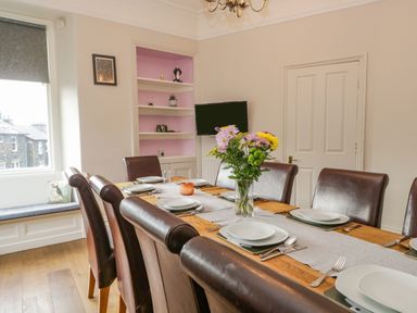 A dining room with a wooden table set for six with plates and cutlery and a vase of flowers at Hollywood in Windermere
