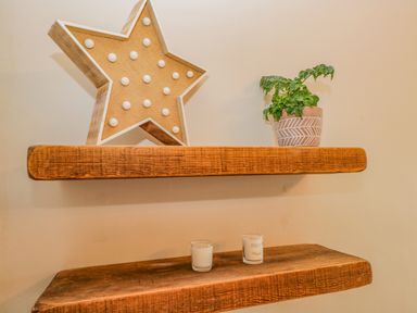 Two wooden shelves on a wall with a star-shaped light and a potted plant on the top shelf and two small candles on the bottom shelf at Hollywood in Windermere