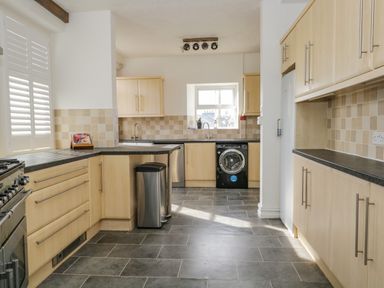 A kitchen with light wood cabinets and black countertops a washing machine a stainless steel trash can and tiled floor at Hollywood in Windermere