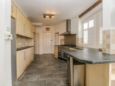 A kitchen with light wood cabinets black countertops a stainless steel stove and oven a range hood and a tiled floor at Hollywood in Windermere