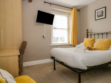 A bedroom with a bed yellow pillows yellow curtain a desk with a chair and a wall mounted television at Hollywood in Windermere