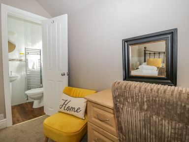 A small corner with a yellow chair and pillow next to a dresser with a mirror and a bathroom visible through an open door at Hollywood in Windermere