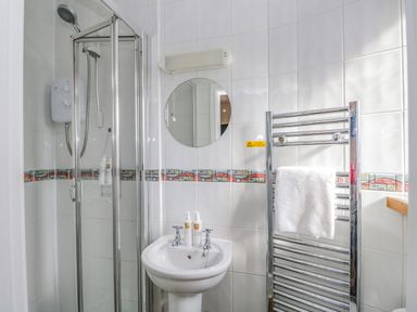 A bathroom with a shower cubicle sink with soap dispensers round mirror and heated towel rail with towel at Hollywood in Windermere