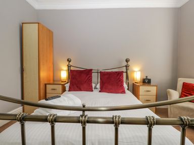 A bedroom with a metal bed frame white bedding two red pillows bedside tables with lamps and a chair at Hollywood in Windermere