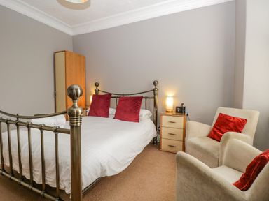 A bedroom with a metal bed frame red pillows a wooden wardrobe two armchairs and a bedside table with a lamp at Hollywood in Windermere
