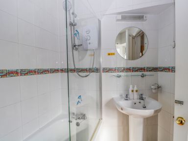 A bathroom with a bathtub and shower unit next to a sink with a mirror above at Hollywood in Windermere