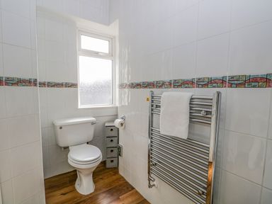 A bathroom with a toilet a window wooden floor and a towel on a wall-mounted radiator at Hollywood in Windermere
