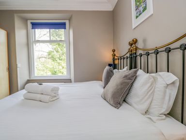 A bedroom with a made bed pillows folded towels window and wardrobe at Hollywood in Windermere
