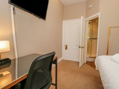 A bedroom with a desk and chair a TV mounted on the wall a bed and an open door leading to a bathroom at Hollywood in Windermere