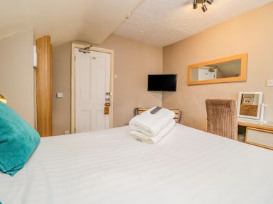 A bedroom with a bed a folded towels a remote control a wall mirror a door a mounted TV and a desk with a chair at Hollywood in Windermere