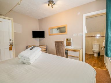 A bedroom with a bed towels and remote on it a wall mounted TV a desk chair and a bathroom in the background at Hollywood in Windermere