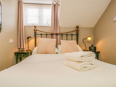 A bedroom with a bed with two beige pillows two folded white towels two bedside tables with lamps and a window behind the bed at Hollywood in Windermere