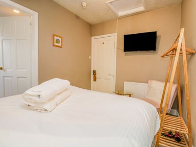A bedroom with a bed and folded towels a wall mounted tv and a wooden clothes rack at Hollywood in Windermere