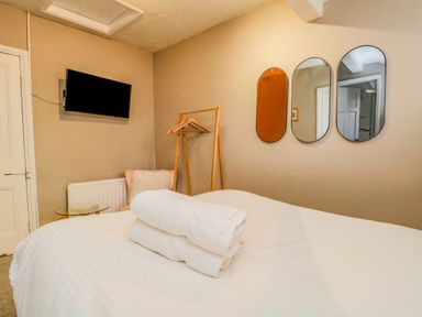 A bedroom with a bed with white linens and towels a wall-mounted TV three mirrors a coat rack and a chair with a side table at Hollywood in Windermere