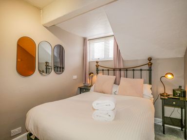 A bedroom with a double bed and pillows folded towels on the bed and three mirrors on the wall at Hollywood in Windermere