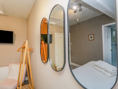 A bedroom with three oval mirrors on a wall a wooden clothes rack a pink chair and a wall-mounted television at Hollywood in Windermere