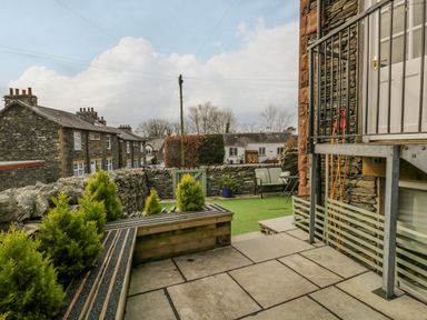 A stone patio with steps and green plants next to a small artificial grass yard with chairs and a stone wall at Hollywood in Windermere