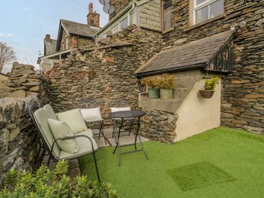 An outdoor seating area with metal chairs and a table on artificial grass surrounded by stone walls at Hollywood in Windermere