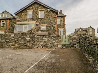 A stone house with a green gate and stone wall in front of a parking area at Hollywood in Windermere