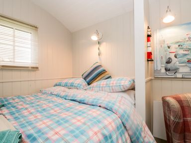 A bedroom with a bed and a window with blinds and a chair at Seashore Shepherds Hut @ Moat Farm in Aldingham near Ulverston
