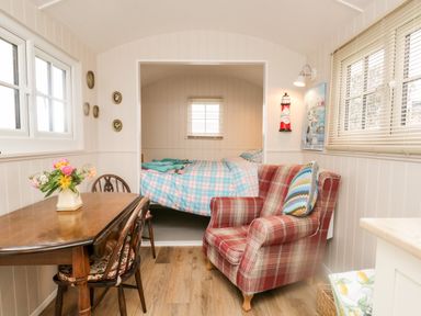 A room with a wooden dining table with chairs a plaid armchair and a bed with plaid bedding at Seashore Shepherds Hut @ Moat Farm Aldingham near Ulverston