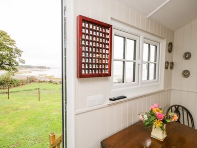 A dining area with a wooden table and flower vase by a window with a remote and a wall display of collectible thimbles at Seashore Shepherds Hut @ Moat Farm Aldingham near Ulverston