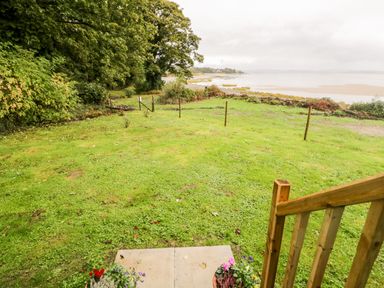 A grassy yard with flowers in pots on a stone step and a view of water and trees at Seashore Shepherds Hut @ Moat Farm Aldingham near Ulverston