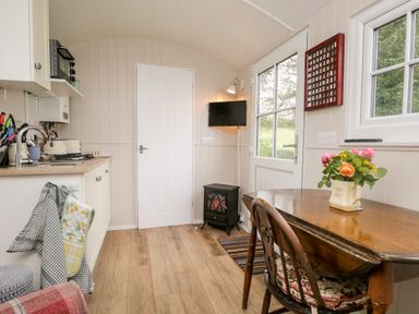 A small kitchen area with a wooden table and chairs and a door with windows at Seashore Shepherds Hut @ Moat Farm in Aldingham near Ulverston