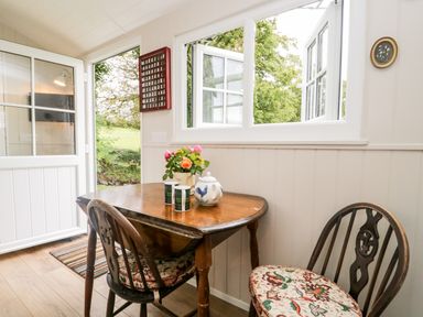 A dining area with a wooden table and two chairs next to an open door and window at Seashore Shepherds Hut @ Moat Farm in Aldingham near Ulverston