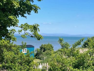 A view of the sea and a blue shed surrounded by trees at Seashore Shepherds Hut @ Moat Farm Aldingham near Ulverston
