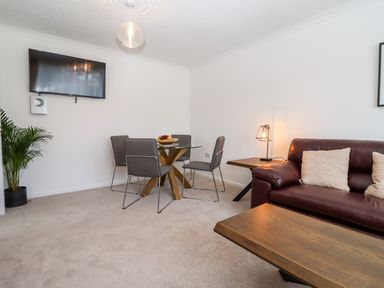 A dining area with a round glass table and four chairs next to a living room with a brown leather sofa and a wooden coffee table at 3 Granbrook Lane in Mickleton Gloucestershire