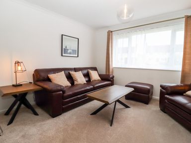 A living room with brown leather sofas cushions a coffee table and a window at 3 Granbrook Lane in Mickleton Gloucestershire