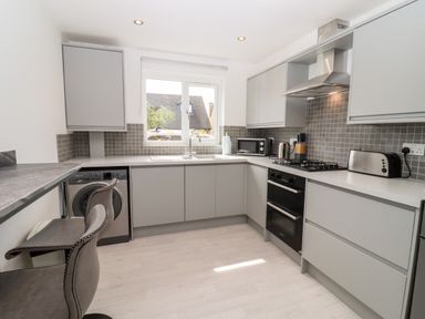 A kitchen with grey cabinets a washing machine oven toaster microwave and bar stools at 3 Granbrook Lane Mickleton Gloucestershire