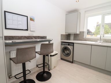 A kitchen with two bar stools by a counter a washing machine and a window at 3 Granbrook Lane Mickleton Gloucestershire